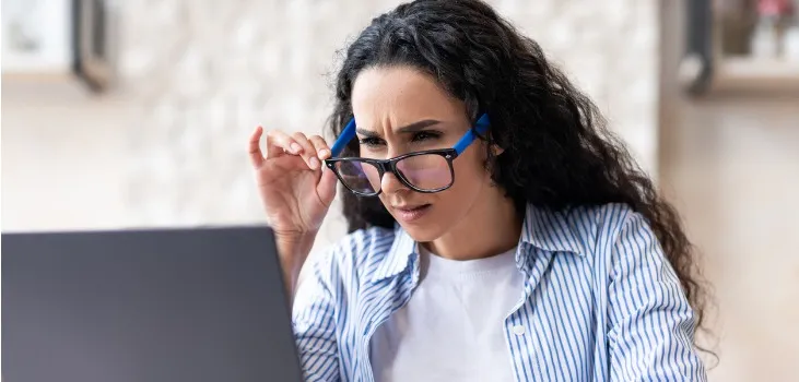 a woman wearing eyeglasses squinting trying to read in her laptop